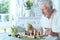 Senior man looking at chess board while drinking tea at home