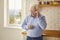 Senior man making a phone call and ordering food delivery while standing in the kitchen