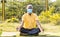 Senior man in medical face mask meditating on yoga mat at park - cconcept of elderly people healthcare, fitness during coronavirus