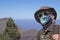 Senior man in medical mask traveling in mountain landscape in Tenerife, horizon over the sea - new normal life concept in active