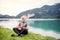 A senior man pensioner sitting by lake in nature, doing yoga exercise.