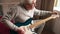 Senior man is playing guitar. Elderly man sitting on the sofa and playing guitar. Portrait of a gray-haired mature man