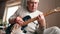 Senior man is playing guitar. Elderly man sitting on the sofa and playing guitar. Portrait of a gray-haired mature man