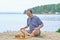 Senior man pondering a move in a game of chess and sitting on the beach near the lake