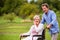 Senior man pushing woman in wheelchair, green autumn nature