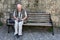 Senior man sits on a bench in front of natural stone masonry