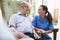 Senior Man Sitting In Chair And Talking With Nurse In Retirement Home