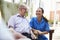 Senior Man Sitting In Chair And Talking With Nurse In Retirement Home