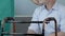 Senior man sitting in front of walking frame, nurse putting hand on his shoulder