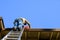 Senior man standing on an aluminum extension ladder cleaning out a roof gutter