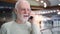 Senior man standing in shopping mall smiling. Using his smartphone, chatting with friends or family