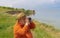 Senior man in straw hat looking into binocular while sitting on Dnipro riverside