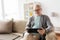 Senior man with tablet pc sitting on sofa at home