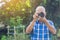 Senior man taking a photo by a digital camera while standing in the park. An elderly Asian man wears a blue shirt be happy when