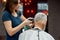 Senior man visiting barbershop. Young professional barber making haircut with hair clipper for mature client. Close up