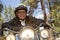 Senior man wearing helmet leaning on motorcycle handlebars in forest