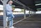 A senior man wearing medical mask due to coronavirus standing under the metal structure of a deserted parking looking at his smart