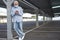 A senior man wearing medical mask due to coronavirus standing under the metal structure of a deserted parking looking at his smart