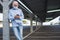 A senior man wearing medical mask due to coronavirus standing under the metal structure of a deserted parking looking at his smart