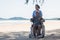 Senior man on wheelchair and elderly woman couple smiling on sand of the beach