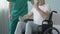Senior man in wheelchair flexing arms with dumbbells, assisted by nurse, rehab