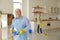 Senior man wipes the shelves holding a washcloth and detergent while his wife washes the floor.