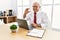 Senior man working at the office using computer laptop smiling and confident gesturing with hand doing small size sign with