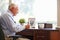 Senior Man Writing Memoirs In Book Sitting At Desk