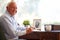 Senior Man Writing Memoirs In Book Sitting At Desk