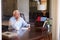 Senior Man Writing Memoirs In Book Sitting At Desk