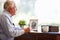 Senior Man Writing Memoirs In Book Sitting At Desk