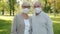 Senior married people wearing face masks standing in park together looking at camera
