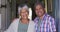 Senior mixed race couple standing in open front doorway smiling to camera