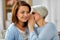 Senior mother whispering to adult daughter at home