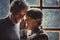 Senior old couple in love at home with snow winter outside the window. Aged woman whisper at man ear. Mature couple enjoy