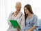 A senior older female doctor visits the patient`s room and explains information on the chart for the patient