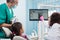 Senior pediatric dentist with assistant doing dental treatment patient girl using dental x-ray machine in dental office