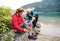 Senior pensioner couple hikers standing by lake in nature, taking shoes off.