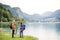 A senior pensioner couple hikers standing by lake in nature, talking.