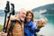 A senior pensioner couple standing by lake in nature, taking selfie.