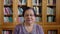 Senior portrait, Indian woman and library with elderly lady glasses and bookshelf behind her. Content, serious and old