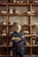 Senior potter standing against shelves with pottery goods at workshop