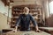 Senior potter standing and leaning on table against shelves with pottery goods at workshop