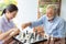 Senior retirement man playing chess with nurse at home