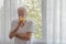 A senior retirement man stand beside room window holding a glass of orange juice look outside with happiness