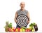 Senior in sportswear holding a target behind a table with vegetables and fruit