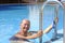 Senior sporty woman smiling out of the pool with swimming goggles and cap in hand - active retiree enjoying swimming on a sunny