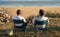 Senior spouses resting in chairs with coffee cups observing ocean