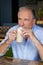 Senior thoughtful man holding cold coffee while sitting at table