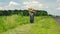 Senior with walking stick carrying heavy sack moving on a roadside at summer season